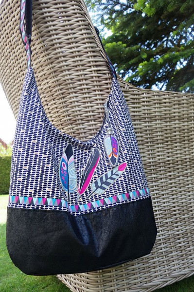 Umhängetasche mit hochgezogenem Taschenboden, aufgenähter Webbandborte und aufgestickten Federn.